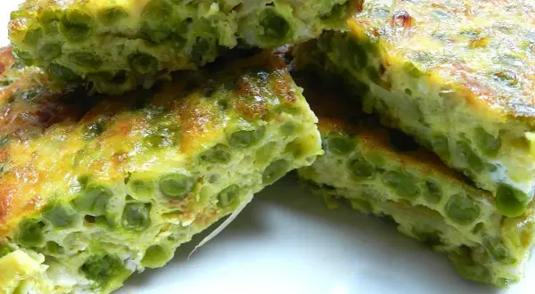 Fette di frittata di piselli, dorata e soffice, con piselli verdi ben visibili nell'uovo.
