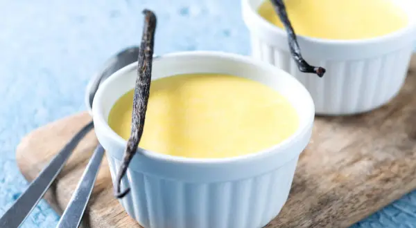 Deliciosas natillas de plátano, cremosas y con un toque de vainilla, servidas en ramequines blancos sobre una tabla de madera.