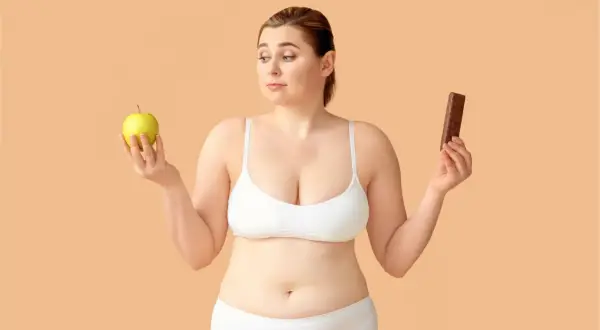 Kobieta w bieliźnie zastanawia się nad wyborem między jabłkiem a batonikiem. Jej figura i stylizacje sugerują dylemat związany z dietą.