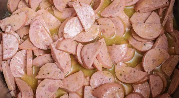 Scheiben von Lyoner Wurst in einer gelben, würzigen Soße, bereit für einen herzhaften Wurstsalat.