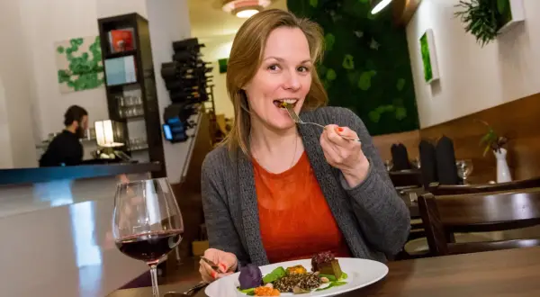 Frau genießt ein veganes Gericht in einem Berliner Restaurant. Auf dem Teller sind bunte Komponenten und ein Glas Rotwein.