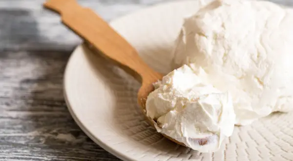 Un cucchiaio di legno raccoglie del cremoso mascarpone da un piatto. Si può congelare il mascarpone per conservarlo più a lungo.