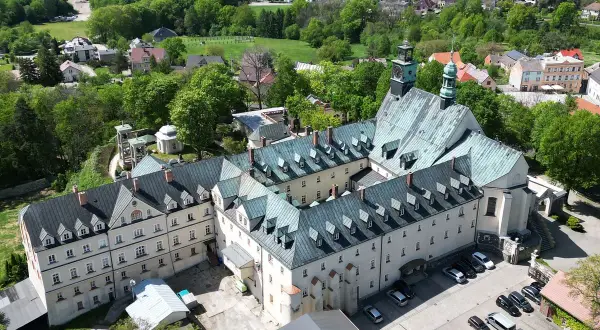 Widok z lotu ptaka na klasztor na Górze Świętej Anny. Rozległy kompleks budynków z zielonymi dachami otoczony bujną zielenią.