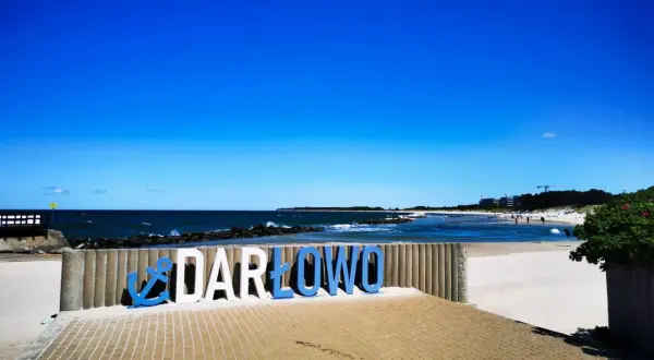 Napis "DARŁOWO" na plaży, zapraszający do odkrywania atrakcji nad Bałtykiem.