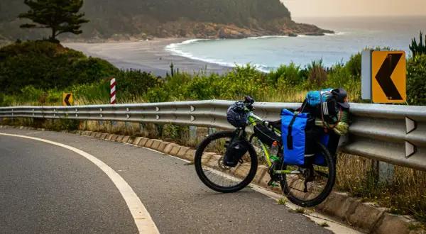 Rower gotowy do bike packingu, obładowany bagażami, stoi przy drodze z widokiem na ocean i plażę.
