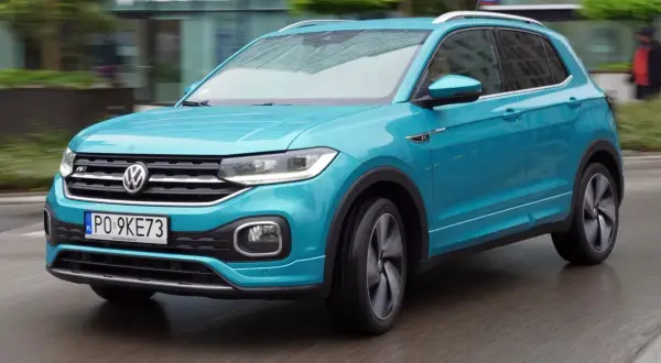 Turkusowy Volkswagen T-Cross w ruchu miejskim, z widocznym numerem rejestracyjnym PO 9KE73.
