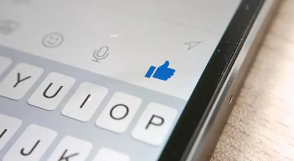 Kciuk w górę na ekranie telefonu, pokazujący, jak działa aktywność na Messengerze. Klawiatura i ikony czatu.