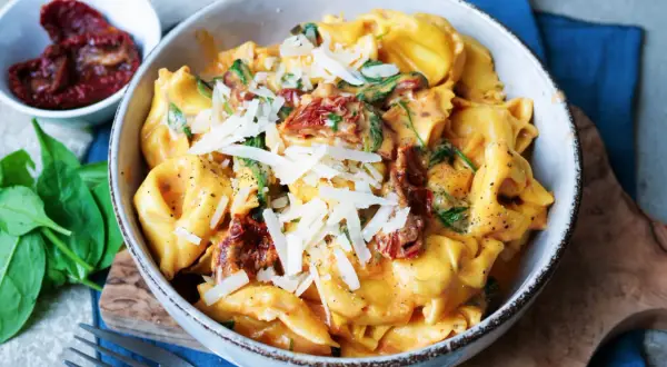 Cremige Tortellini mit Spinat und getrockneten Tomaten, bestreut mit Parmesan. Ein köstliches Gericht, das Lust auf mehr Tortellini Rezepte macht.
