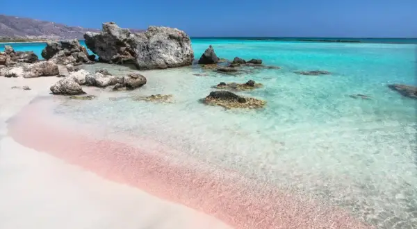 Różowy piasek na Elafonisi Beach, turkusowa woda i skały tworzą rajski krajobraz.