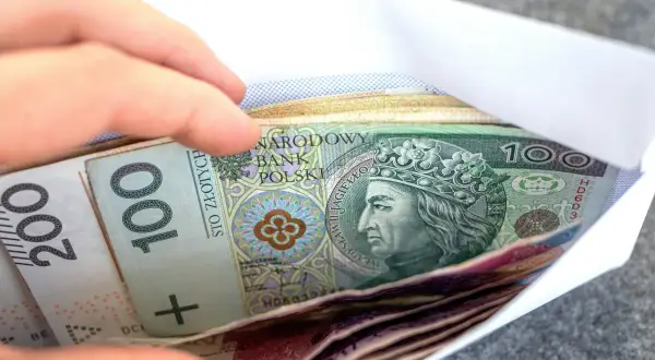 Dłoń wsuwa kopertę z banknotami 100 i 200 zł. Zastanawiasz się, renta wdowia komu przysługuje?