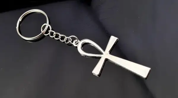 Srebrny brelok z symbolem ankh, starożytnym egipskim znakiem życia, na czarnym tle.