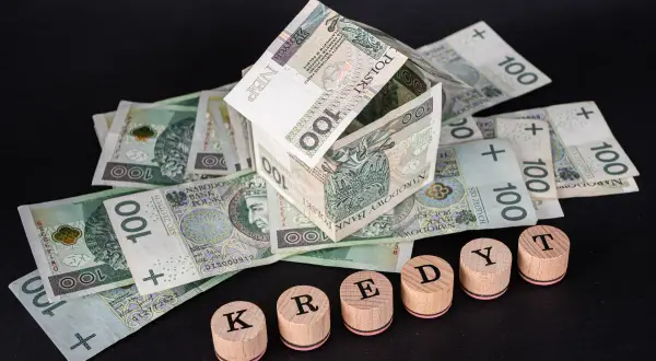 Dom z banknotów 100 zł i drewniane klocki z napisem "KREDYT". Uważaj na najczęstsze błędy w umowach pożyczkowych, które wykluczają z udziału w losowaniu.