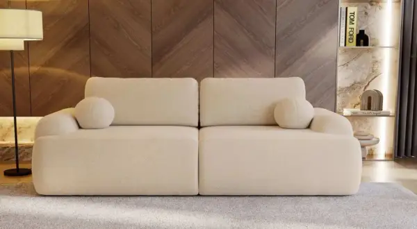 Eine cremefarbene Couch mit runden Kissen, die zum Entspannen einlädt. Sie steht vor einer Holzwand und einem Regal mit Büchern und Deko.