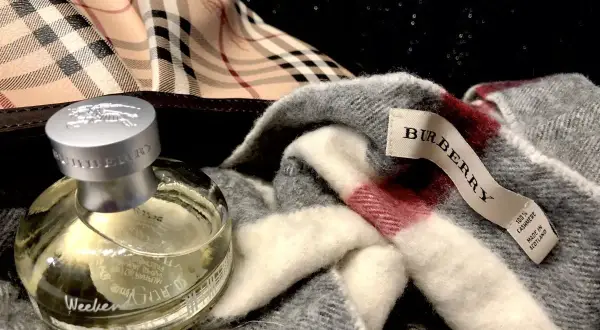 Flakon perfum Burberry Weekend obok szarego szala z charakterystyczną kratą. Idealny zestaw na weekend.