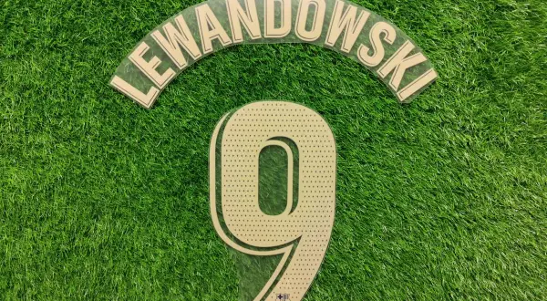 Numer 9 z nazwiskiem Lewandowski i logo Barcy na zielonej murawie.