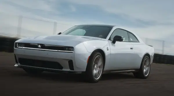 Biały Dodge Challenger Hellcat pędzi po torze wyścigowym, jego sylwetka jest dynamiczna i agresywna.