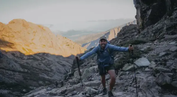 Un randonneur souriant sur un sentier rocheux, bâtons en main. Il semble se demander quel est le gr le plus difficile.