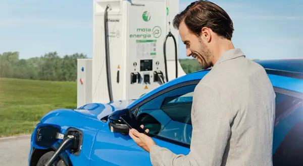 Mężczyzna sprawdza na telefonie koszt ładowania samochodu elektrycznego przy stacji Moja Energia.