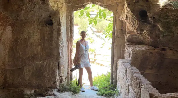 Una donna in abito bianco, con una macchina fotografica in mano, esplora antiche rovine. Un momento di travel photography.
