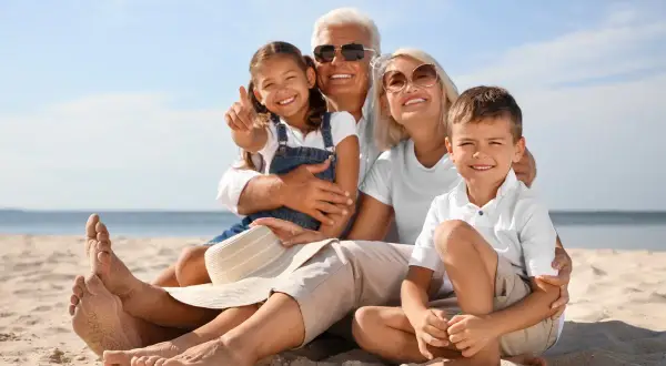 Famiglia felice in spiaggia, i nonni si godono il sole mentre i figli sono in vacanza con loro.