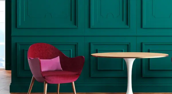 Poltrona rossa vellutata con cuscino rosa, accanto a un tavolino rotondo, su sfondo verde petrolio con pannelli decorativi.