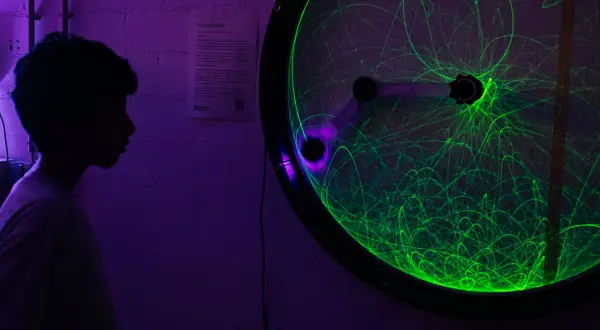 Ein Junge bestaunt ein Doppelpendel mit grünen Lichtspuren bei der Nacht der Wissenschaft Berlin.