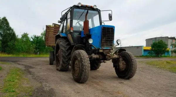 Niebieski traktor z przyczepą pełną siana, gotowy do pracy. Traktorzysta pewnie zaraz ruszy w pole.
