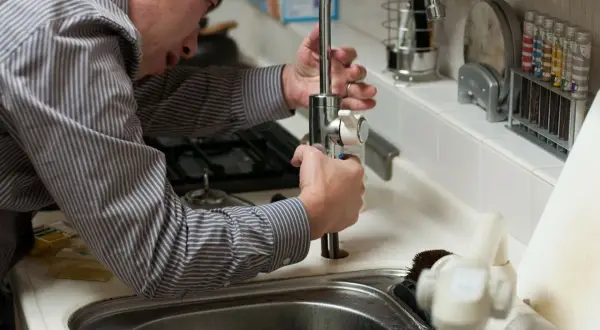 Mężczyzna w koszuli naprawia kran w kuchni.