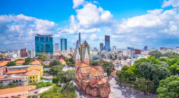 Piękna pogoda w Ho Chi Minh: katedra Notre Dame i nowoczesne wieżowce na tle błękitnego nieba z chmurami.