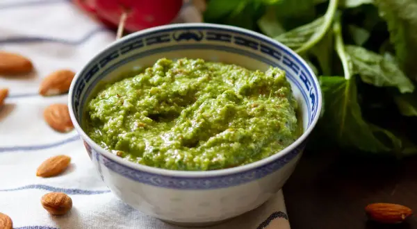 Pesto z liści rzodkiewki, z migdałami i świeżymi ziołami, w miseczce z niebieskim wzorem.