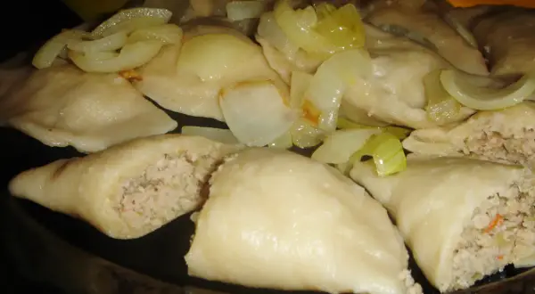 Pyszne pierogi z mięsem i kapustą, polane podsmażoną cebulką, kuszą swoim domowym wyglądem.