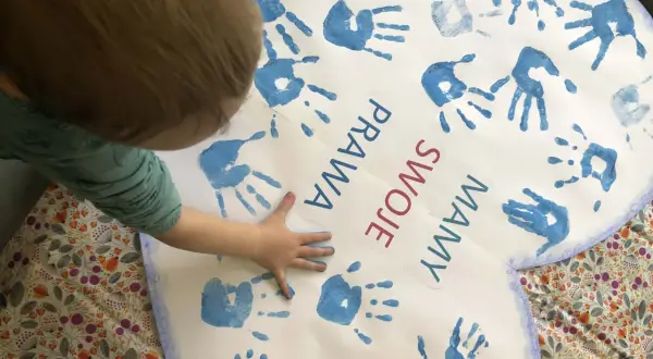 Dziecko tworzy kolaż z odcisków dłoni na sercu z napisem "Prawa swoje mamy".