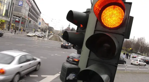 Pomarańczowe światło na sygnalizatorze drogowym. Ruch uliczny w mieście, samochody czekają na zmianę świateł.