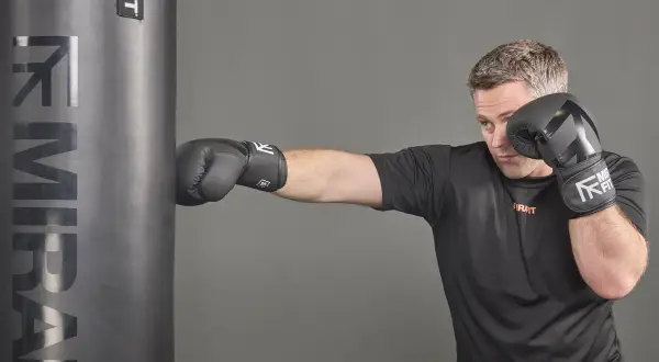 Man in boxing gloves punches a heavy bag, showcasing the full-body workout and the muscles boxing works.