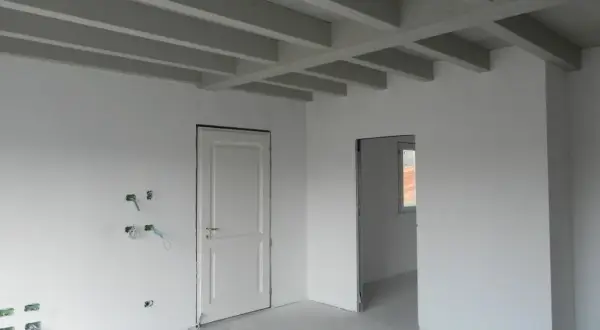 Interno in fase di finitura: pareti bianche, travi a vista e predisposizioni elettriche. Lo spessore intonaco interno è uniforme.