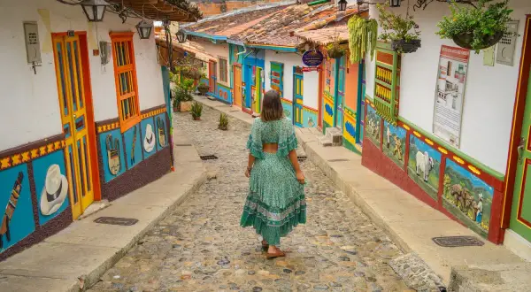 Una mujer camina por una calle empedrada entre casas coloridas, un ejemplo vibrante de los pueblos de Colombia.