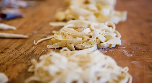 Frische Pasta, bereit für ein köstliches Pasta fresca Rezept, liegt auf einem Holztisch.