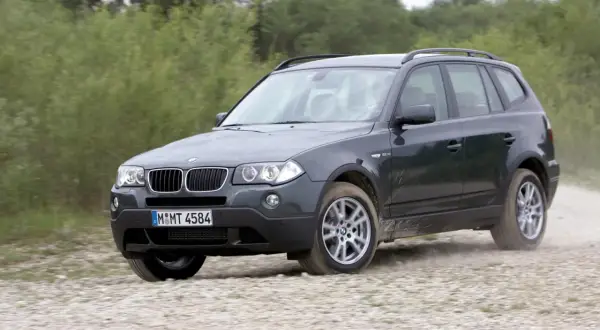 Ciemnoszary BMW X3 E83 pokonuje szutrową drogę, unosząc kurz.