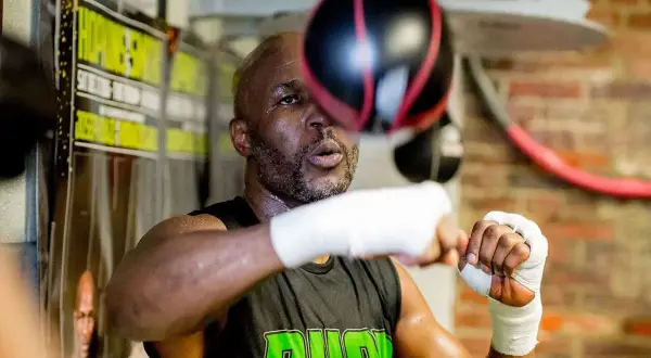 A young Bernard Hopkins, sweat glistening, trains intensely with a speed bag in a boxing gym.