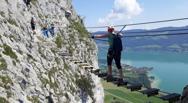 Klettersteig an der Drachenwand bei Mondsee. Wanderer überqueren eine Hängebrücke mit Blick auf den See.
