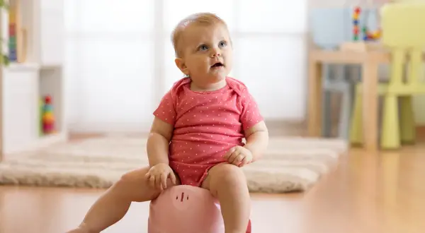 Małe dziecko w różowym body siedzi na różowym nocniku, ucząc się samodzielności.