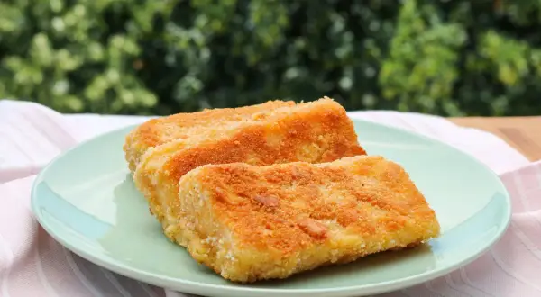 Zwei goldbraun gebackene Emmentaler-Schnitzel auf einem hellgrünen Teller, serviert mit einem rosafarbenen Tuch.