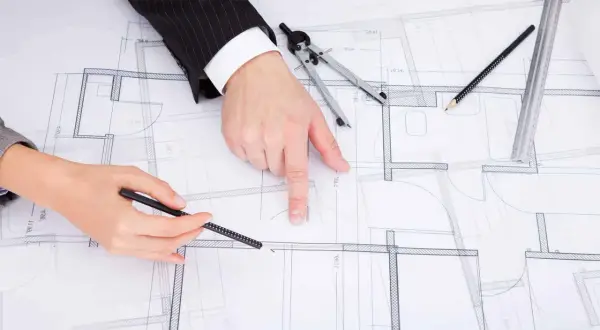 Rysunki techniczne domu, na których dwie osoby omawiają zmianę projektu po uzyskaniu pozwolenia na budowę.