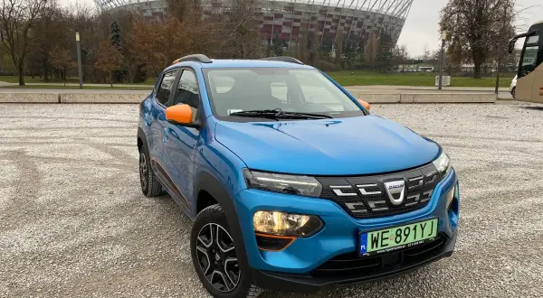 Niebieska Dacia Spring z pomarańczowymi akcentami na tle Stadionu Narodowego. Dacia Spring opinie – miejski elektryk gotowy na przygodę.