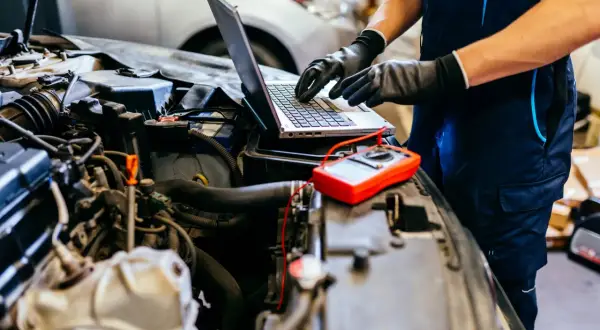 Mechanik diagnozuje problem z silnikiem 4t, który się dusi po dodaniu gazu. Na laptopie analizuje dane, obok leży multimetr.