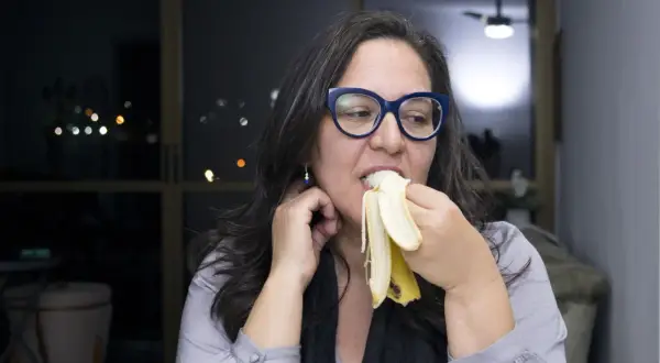 Kobieta w okularach je banana na noc, ciesząc się smakiem.