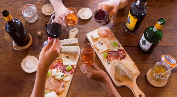 Hände reichen sich Gläser mit Portwein, dazu gibt es Brot, Käse und Aufschnitt. Was ist Portwein? Ein süßer, aufgespriteter Wein aus Portugal.