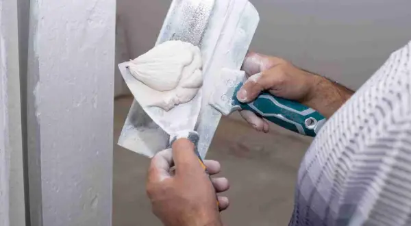 Application d'enduit de lissage sur un mur. Le temps de séchage est crucial avant le ponçage pour un fini parfait.