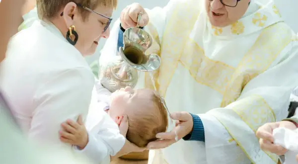 Chrzest dziecka w kościele, ksiądz polewa głowę niemowlęcia wodą z kociołka.