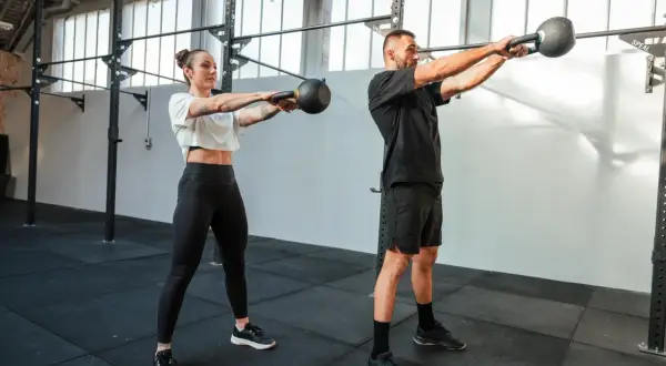 Kobieta i mężczyzna ćwiczą z kettlebellami w siłowni.